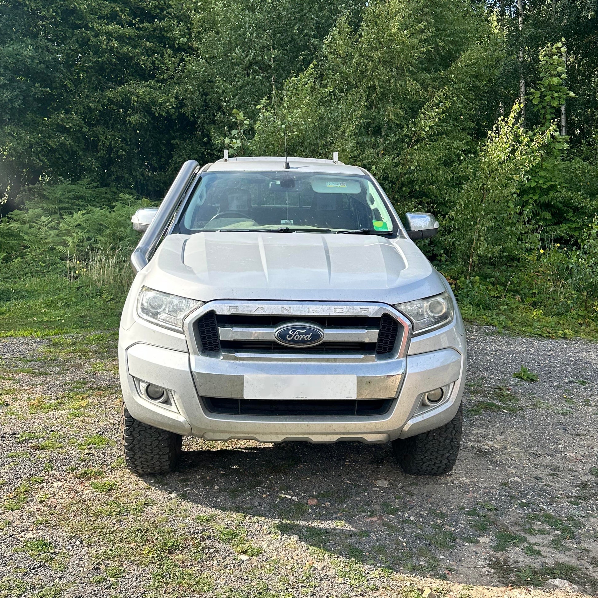 Silver Ford truck parked on a gravel area with trees in the background